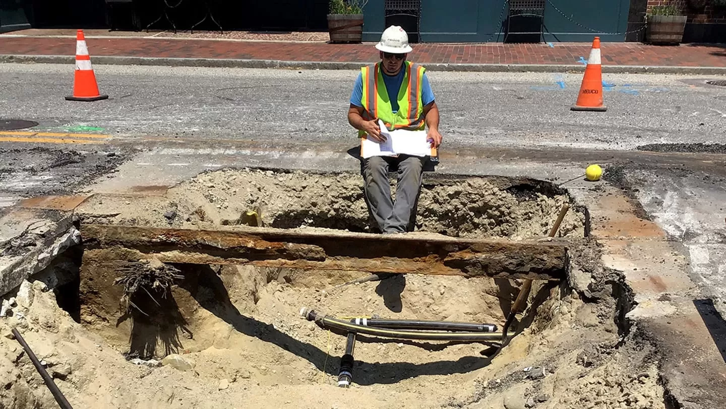 Neuco worker reading over instructions while sitting in a large hole in street