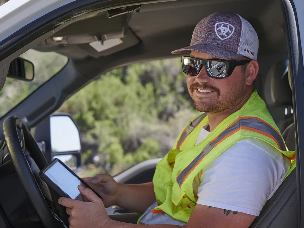 Truck Driver in parked truck with open door holding tablet