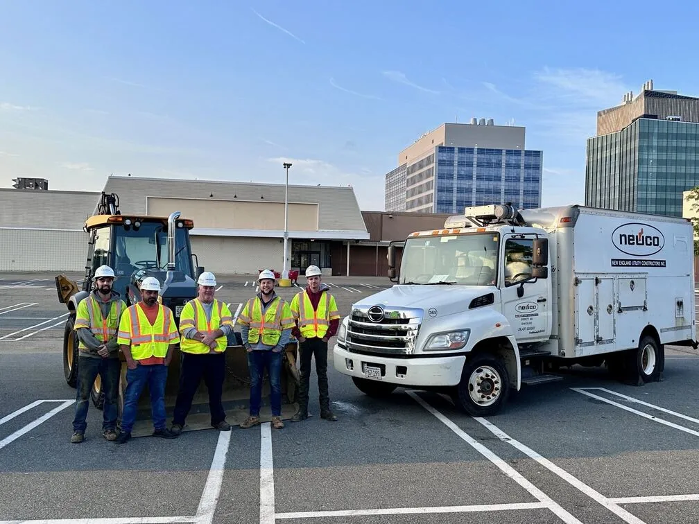 group of five construction workers by a truck and excavator