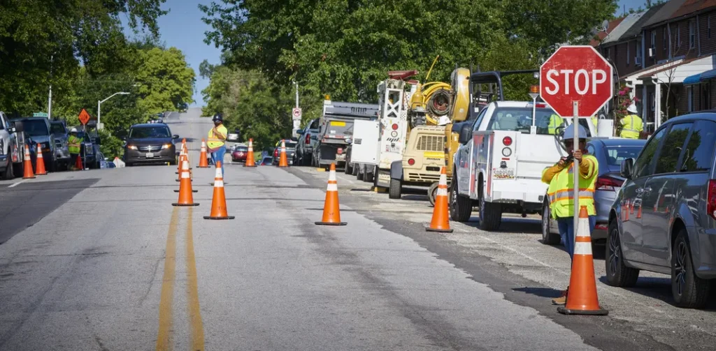 construction crew working on the road. there are cones lined on the road and a worker holding a stop sign for any passing cars.
