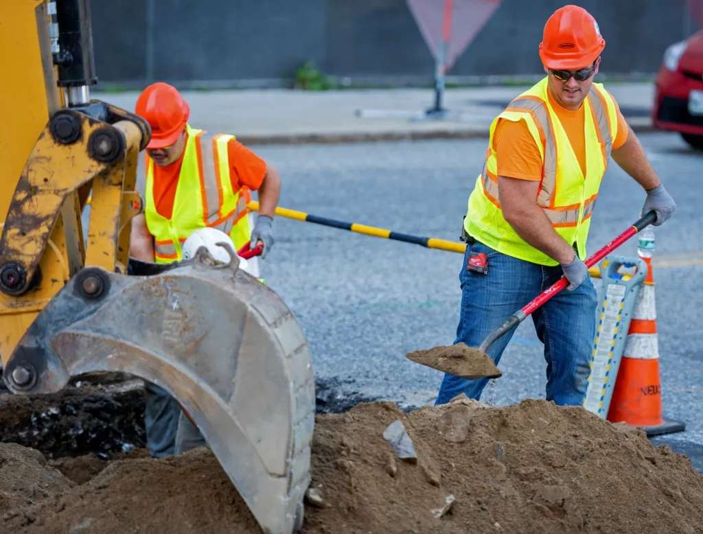 two workers shoveling dirt and a close view of excavator