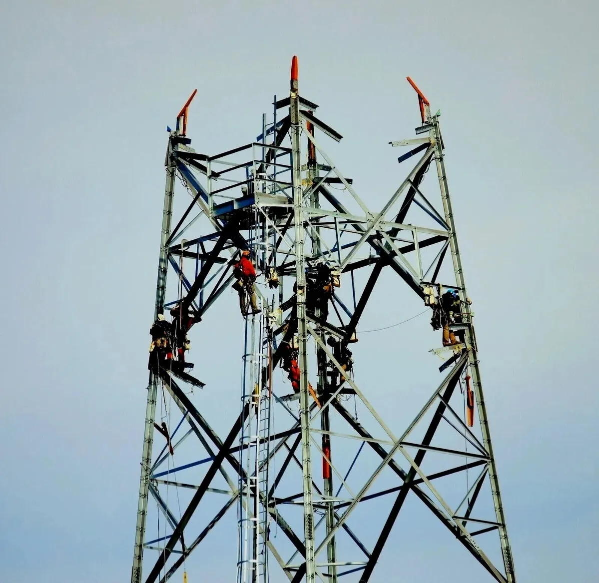Workers in safety gear performing maintenance on a large metal telecommunication tower.