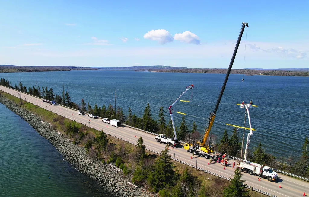 Utility trucks and cranes performing work on a causeway over a large body of water.
