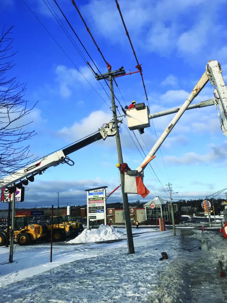 Utility workers in two bucket trucks repairing a power pole on a snowy day.