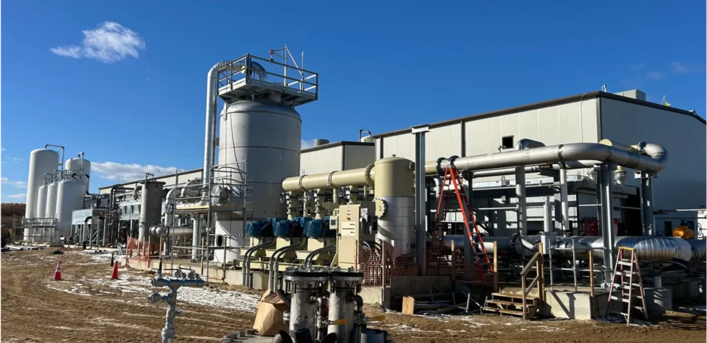 An industrial facility featuring a complex network of silver and beige pipes, large vertical storage tanks, and various processing units under a clear blue sky.