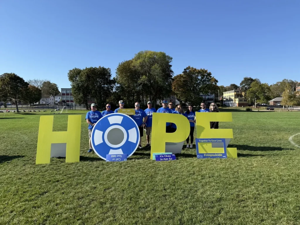 Group of people in blue "HOPE" shirts standing behind large, yellow letters that spell "HOPE".